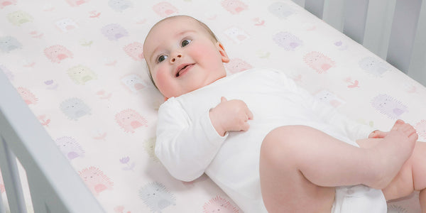 cute baby in a cot with a pink sweet hedgehog print fitted sheet